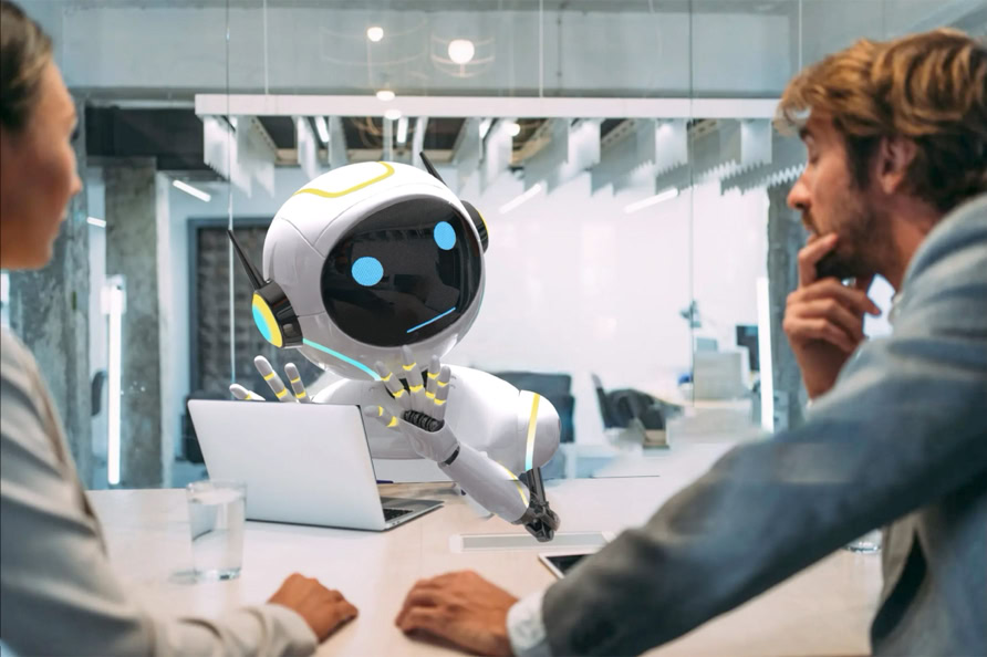 A robot with a screen face and blue eyes sits at a table with two people, one on each side, in an office setting.