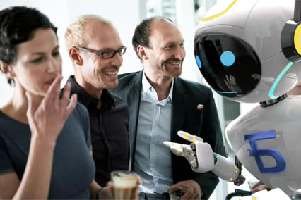 A group of three people interacting with a humanoid robot, with one person holding a drink.